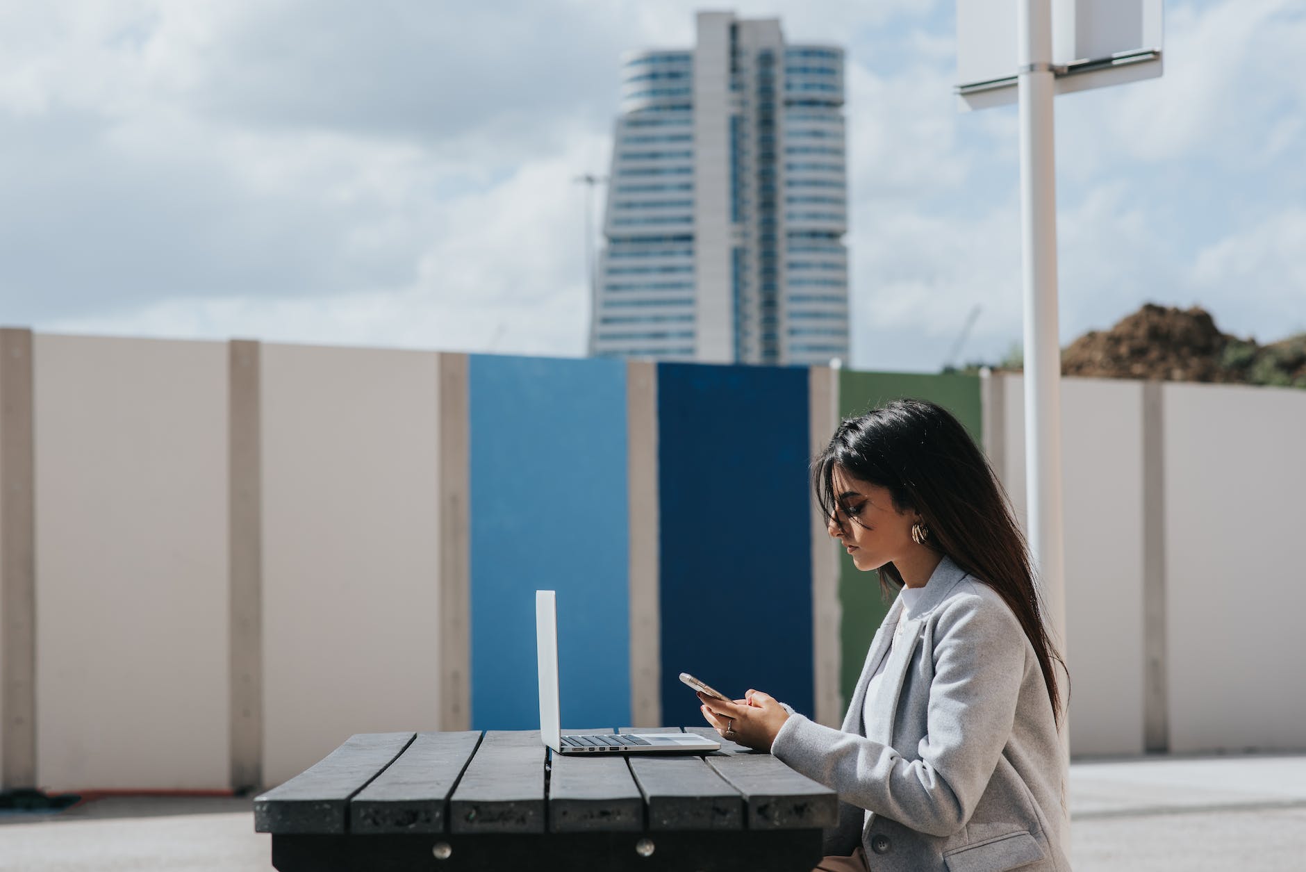 ethnic female executive watching smartphone at table with laptop outdoors