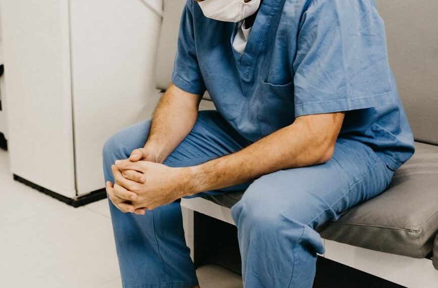 man wearing blue scrub suit and mask sitting on bench